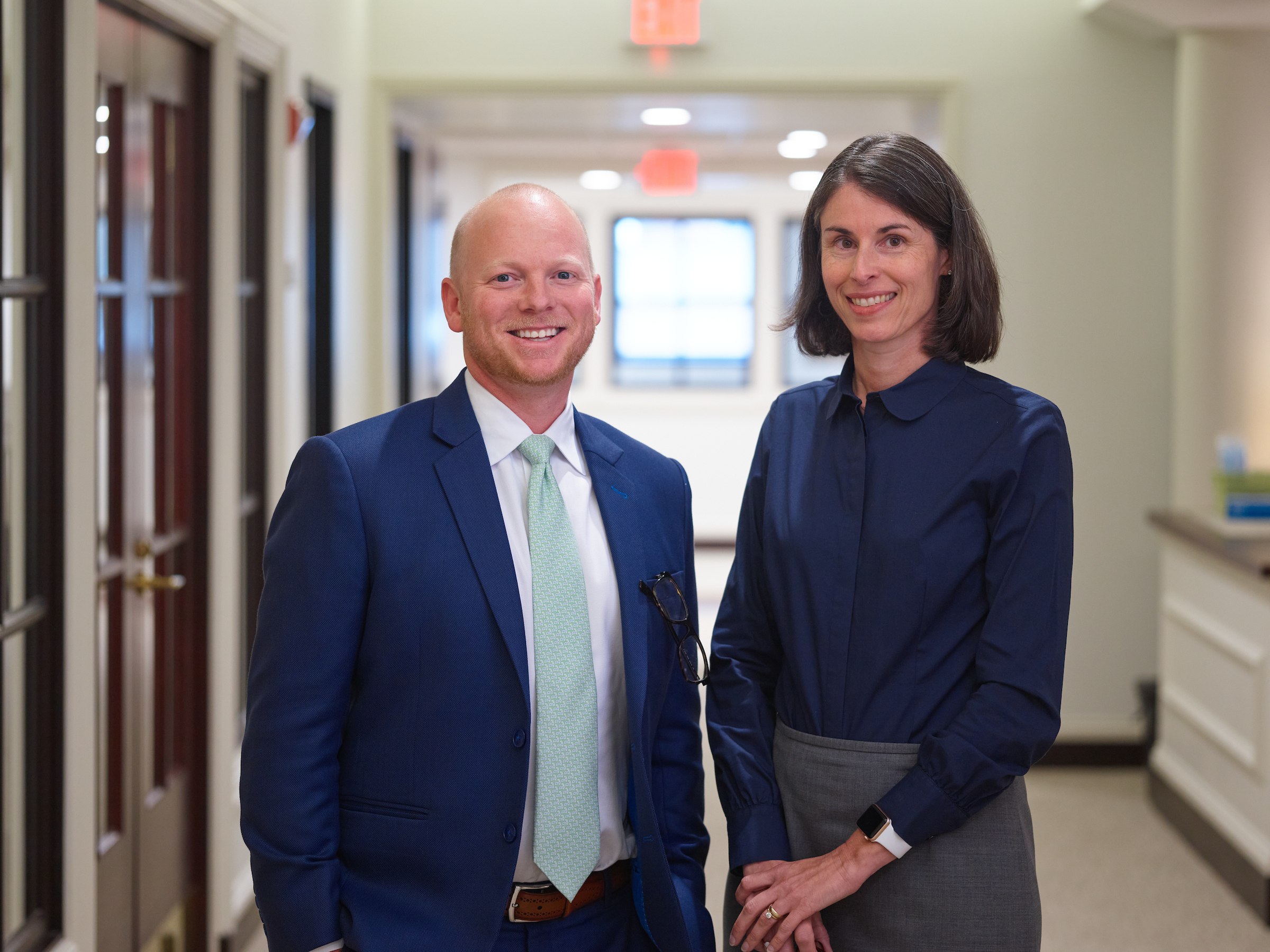 A man and woman in business attire in the hallway of an office